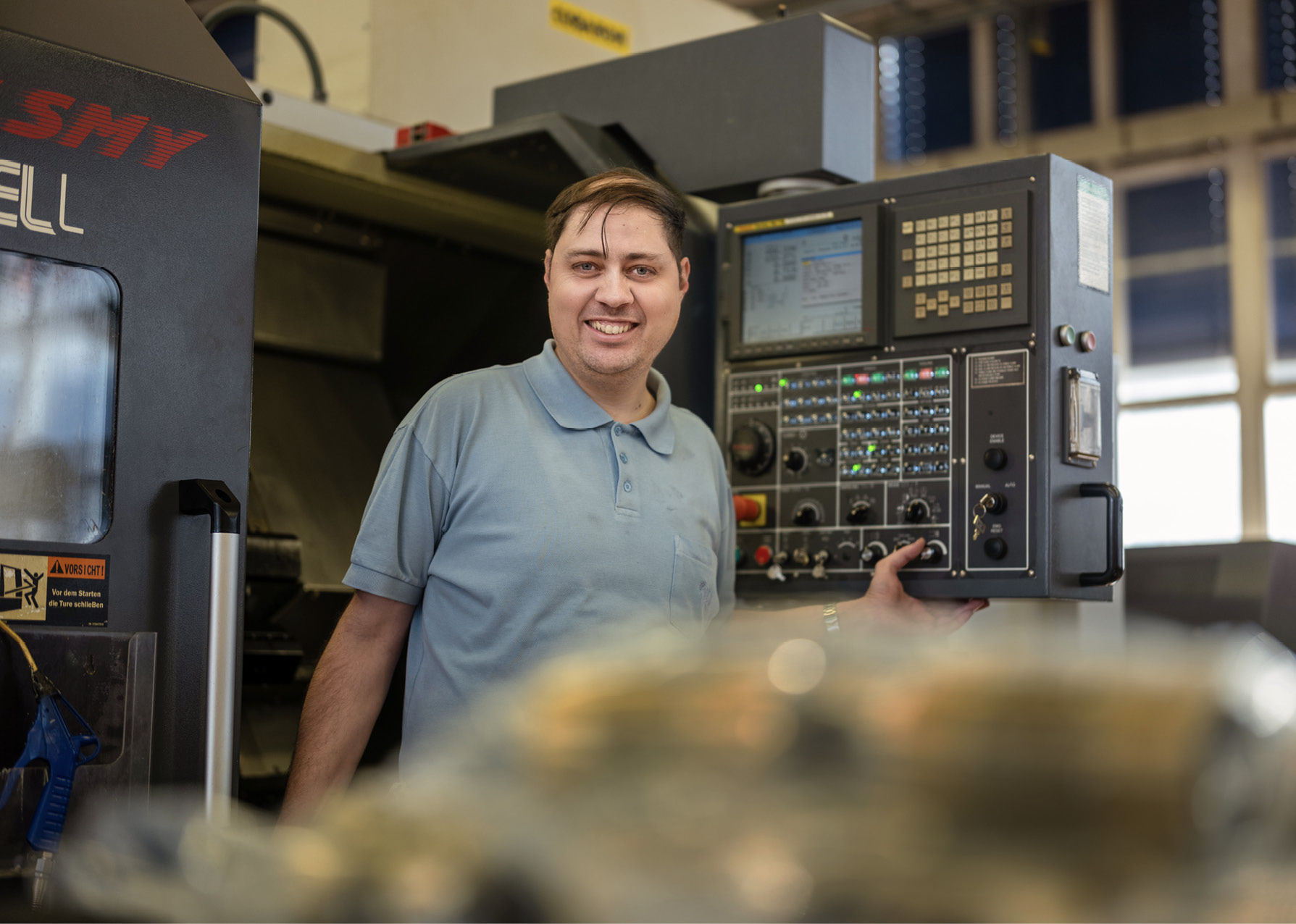 Ein strahlender Mitarbeiter aus dem Team Mechanik, welcher gerade eine Maschinensteuerung bedient.