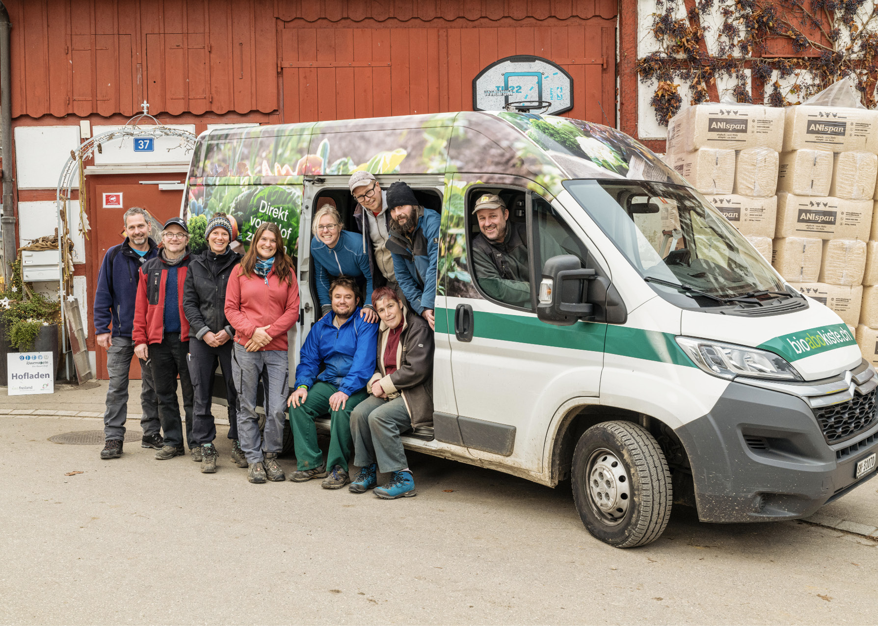 Gruppenbild des gesamten Teams vom Bio-Bauernhofe Löwenstein. Einige Personen sitzen im Lieferwagen oder schauen aus dem Lieferwagen der beliebten Bioabokiste – frisches Gemüse direkt zu Ihnen nach Hause geliefert.