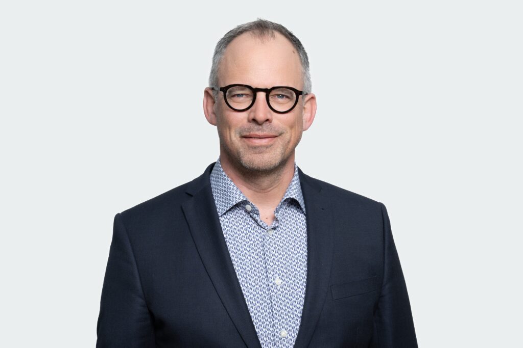 Emanuel Gross, Bereichsleiter Finanzen, Controlling und ICT. Trägt Brille, blauen Veston und blau gemustertes Hemd.