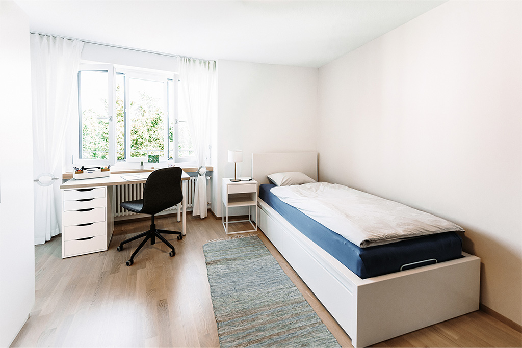 Helles Zimmer mit Bett, Nachttisch und Bürotisch mit Stuhl