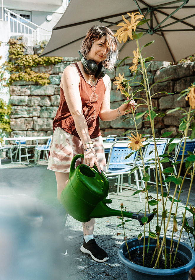 Eine Frau mit einem roten T-Shirt giesst hohe gelbe Blumen