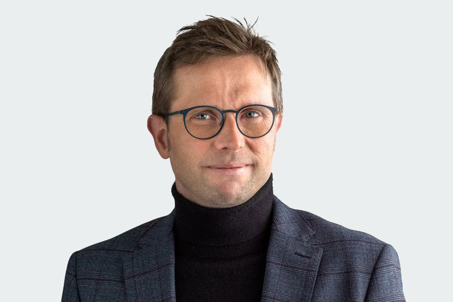 Man with dark turtleneck sweater, gray jacket and glasses. His name is Christoph Hak. He is one of three job coaches at Altra.