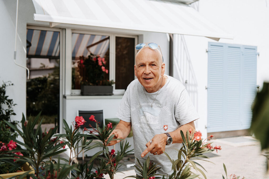 A man with a gray T-shirt and upturned sunglasses standing in front of a raised bed of plants in the seating area of the community garden.