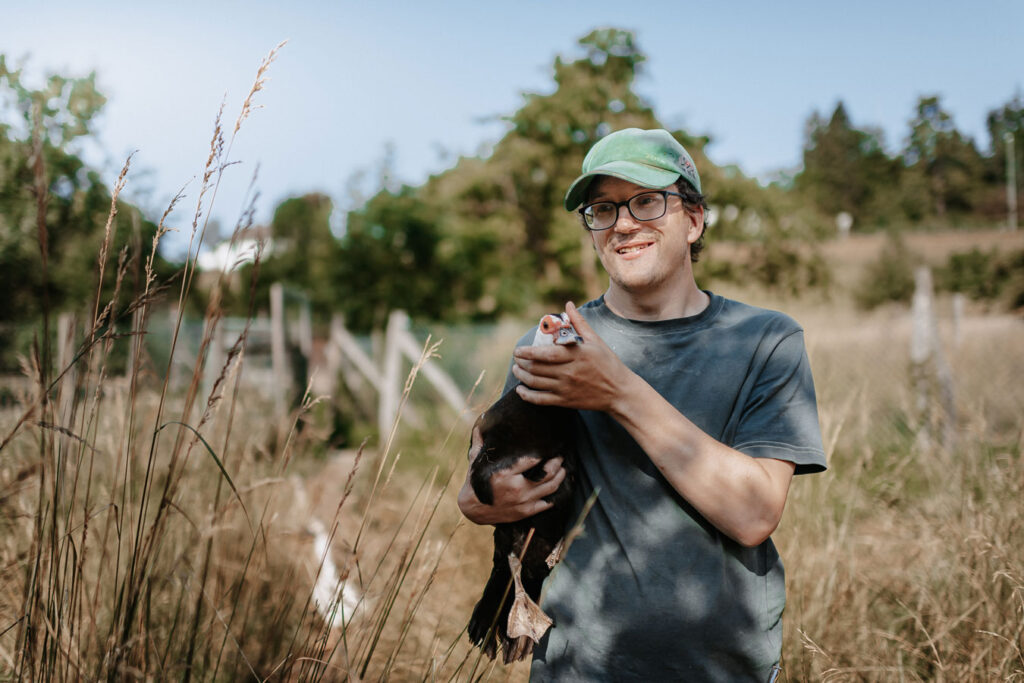 Junger Mann mit grüner Baseball-Kappe und Brille mit einer Ente auf dem Arm.