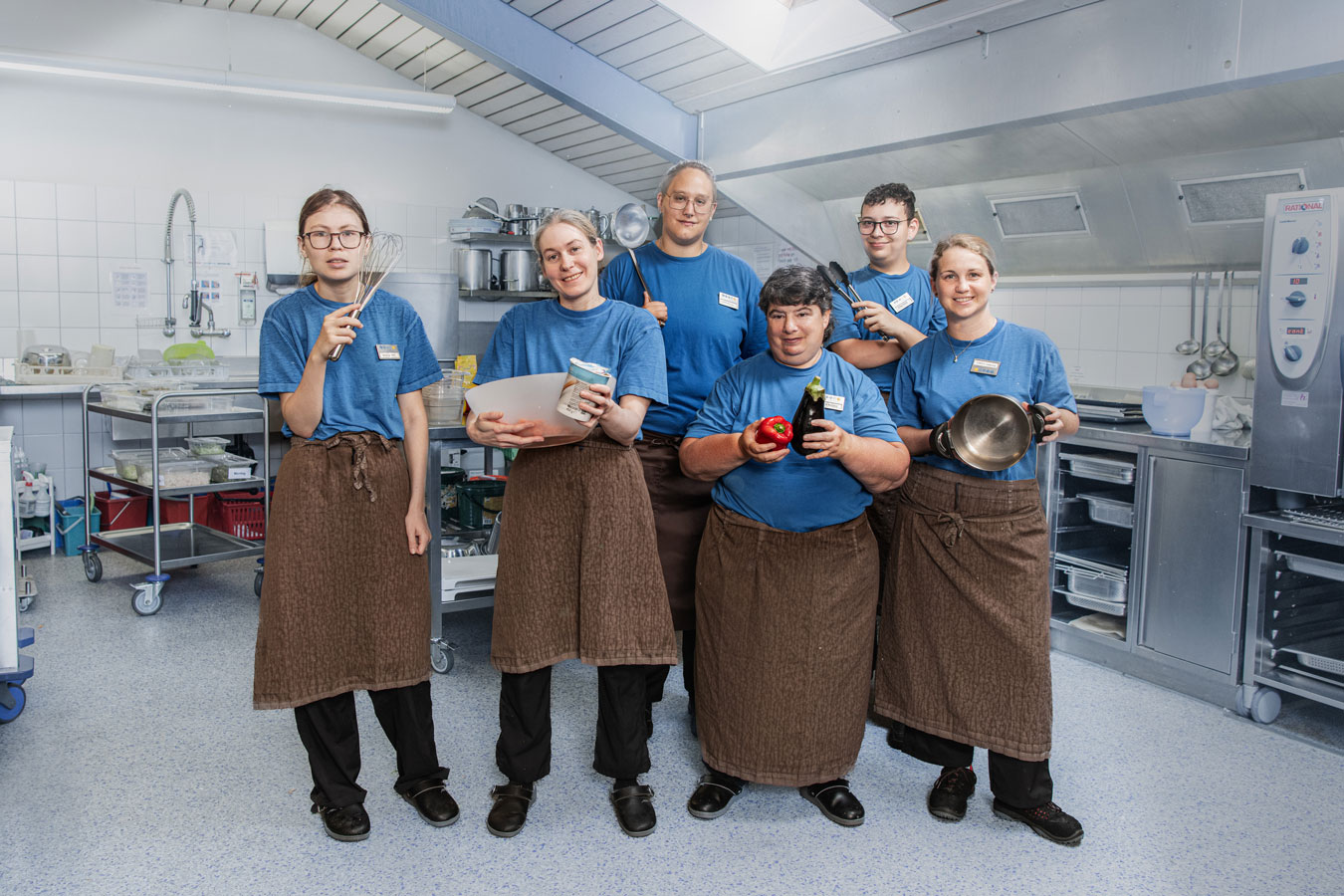 Bild mit 6 Personen des Teams Bistretto. Sie befinden sich in der Küche und haben alle einen Gegenstand in der Hand, z. B. Kochtopf, Schöpflöffel, Schwingbesen.