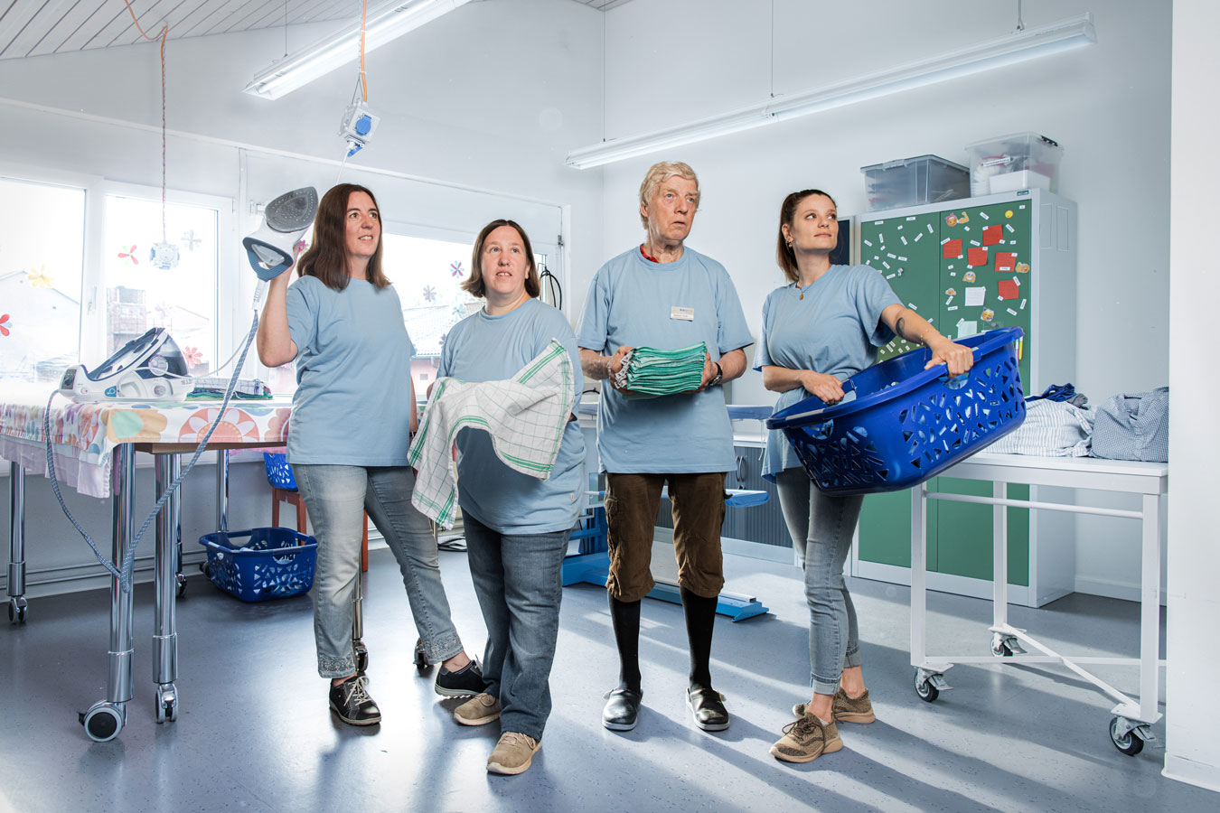 Bild mit 4 Personen des Teams Hauswirtschaft. Personen haben Bügeleisen, Wäsche oder Wäschekorb in der Hand.