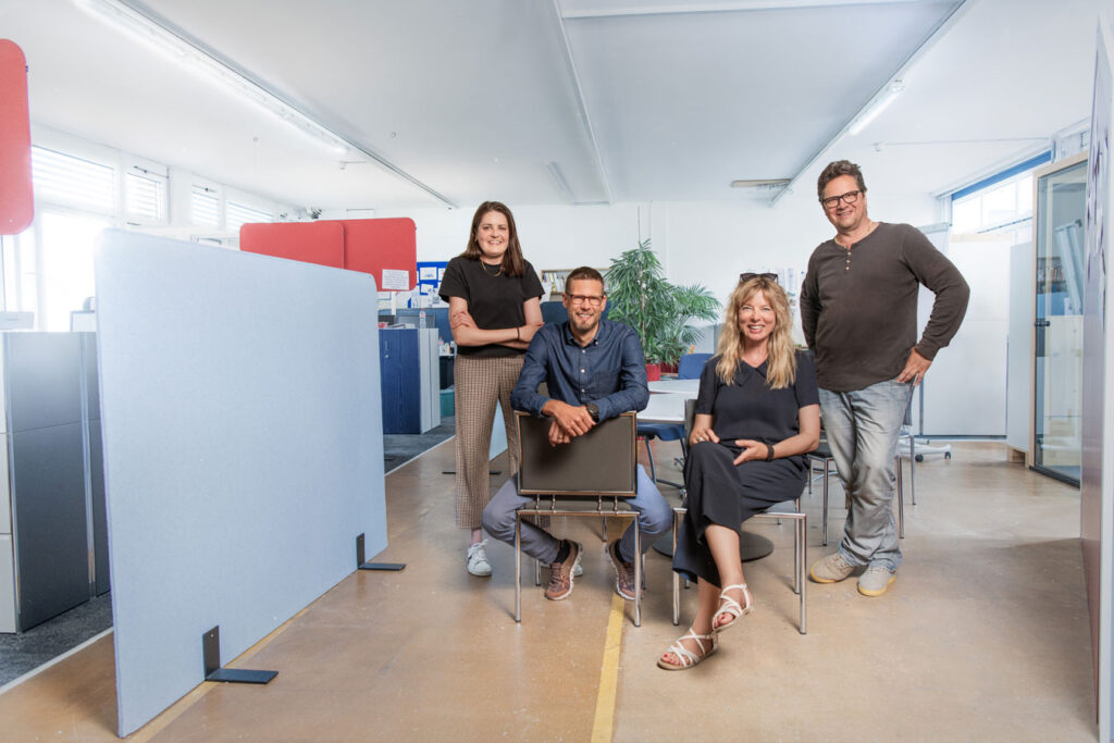 Four people, two sitting, two standing in an office.