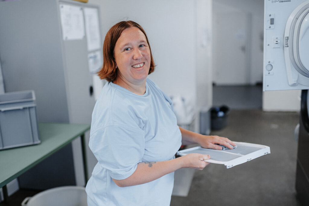 A woman wearing a blue T-shirt cleans a lint filter of a clothes dryer.