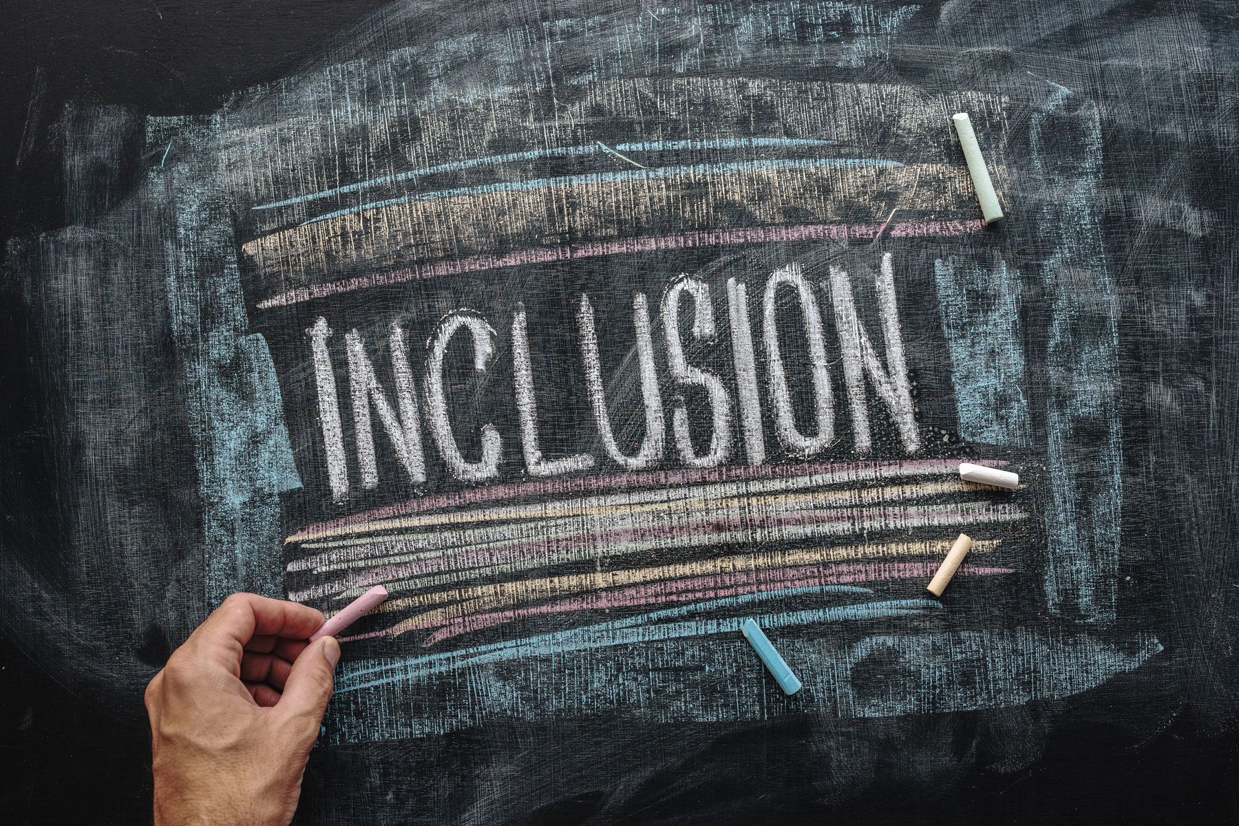 A dark blackboard on which the word INCLUSION was written with chalk in white letters. With different colors the word was colorfully outlined.