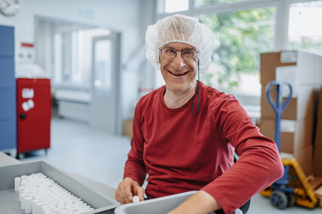 An employee in a dark red long-sleeved shirt and cap closes mini cans.