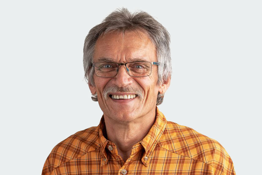 Man with yellow-orange checkered shirt, glasses and moustache. His name is Thomas Maier. He is the head of the apprentice department.