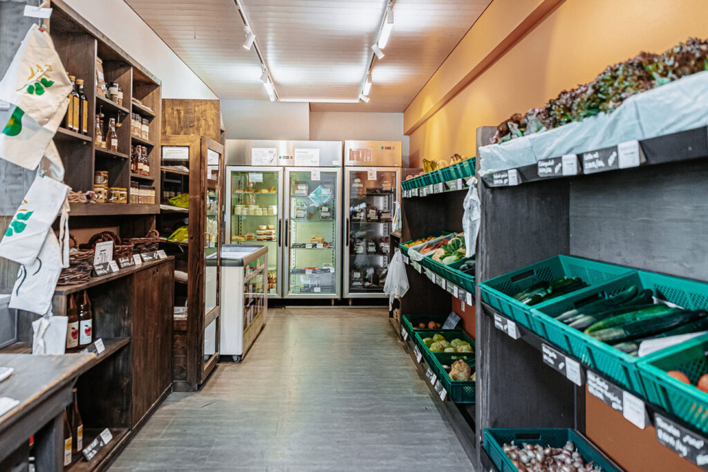 Insight into the farm store, where fresh vegetables and fruit can be bought. Three refrigerators with various agricultural products in the background.