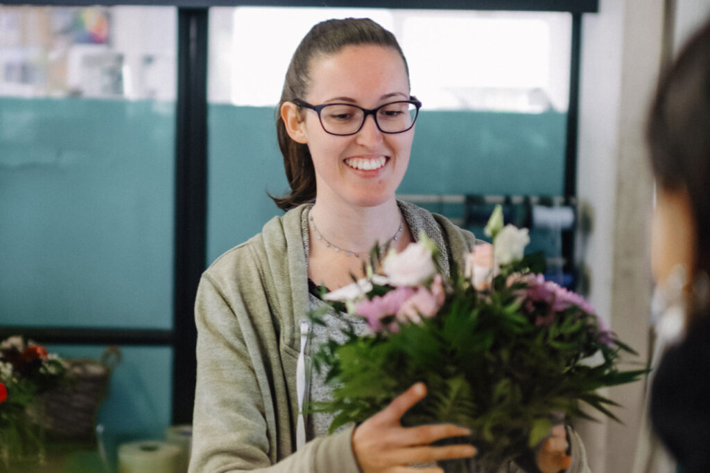 A woman holds a bouquet of flowers in her hand. The flowers are white, pink and purple.