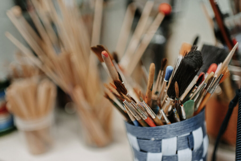 A colorful picture with a cup in which there are many different brushes.