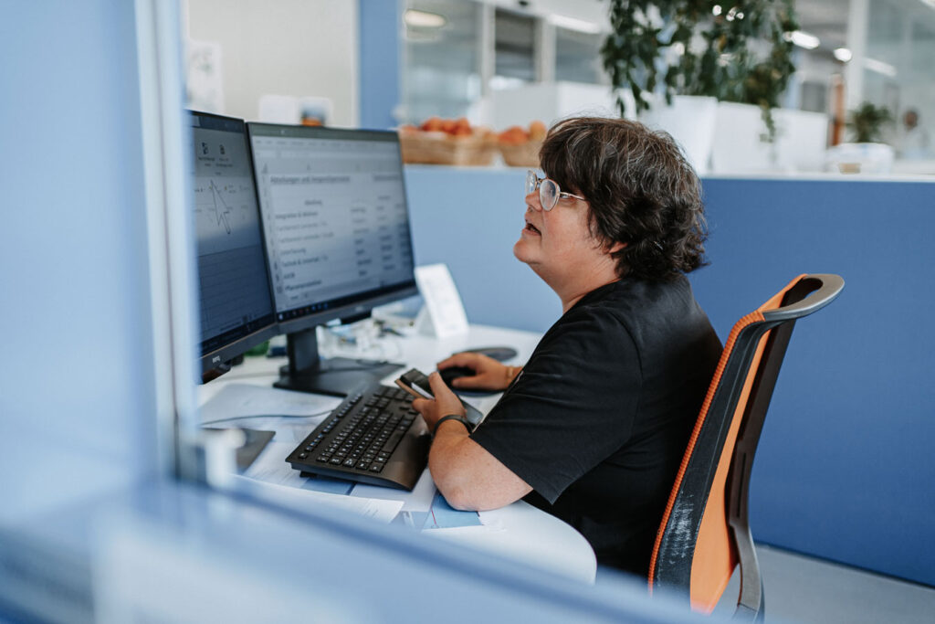 Woman at an office workstation with two screens entering data.