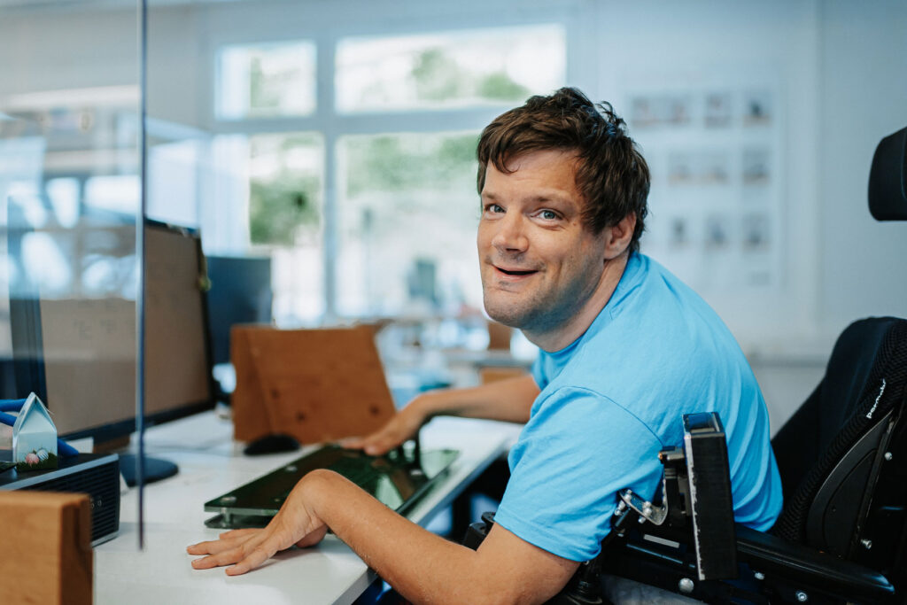 Ein Mann mit blauem T-Shirt blickt von seinem Büro-Arbeitsplatz auf.