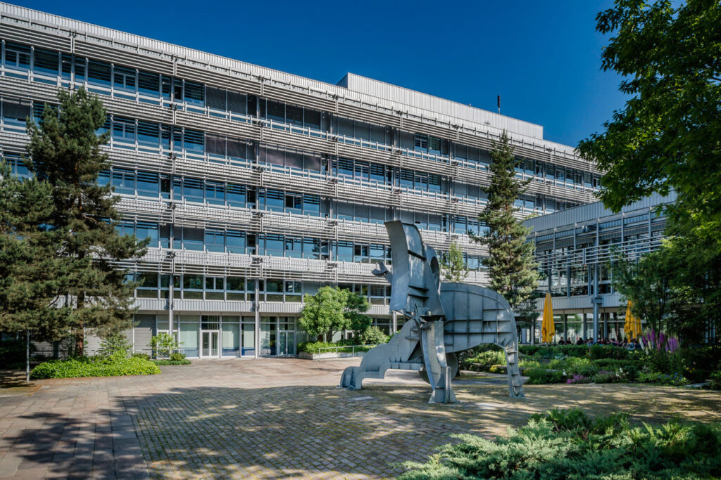 A large office building with many windows and a large sculpture in front of it.
