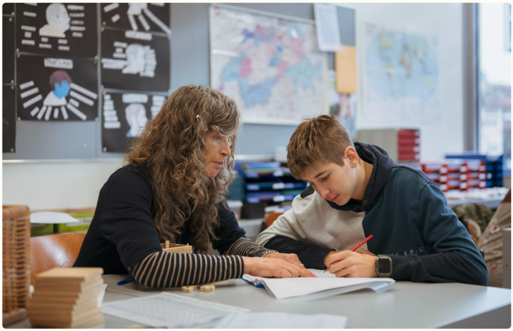 Lehrerin und Schüler sitzen am Schreibtisch und tauschen sich aus.