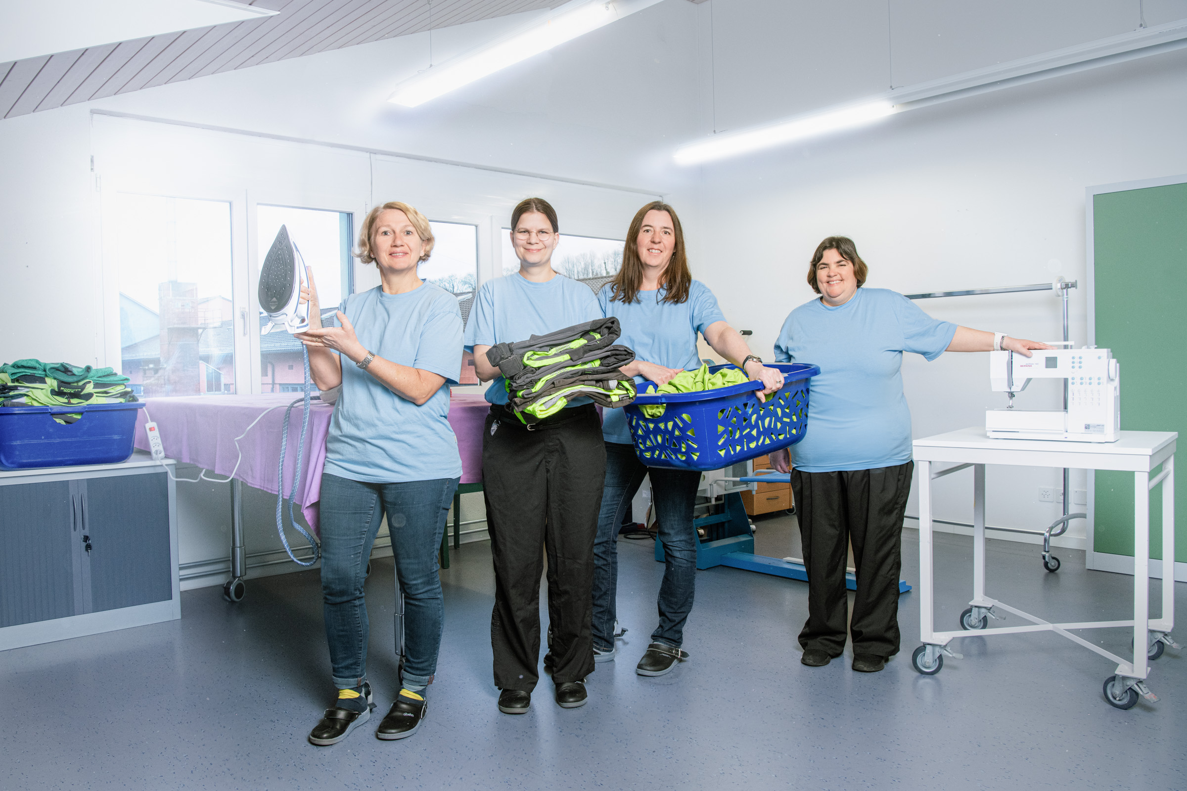 Four people from the housekeeping team. They hold irons, laundry or a laundry basket in their hands.