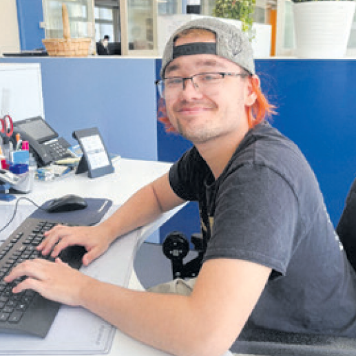 Ein junger Mann trägt eine Mütze und sitzt an einem Schreibtisch